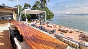 A wooden bar with seating, a covered outdoor area, and a view of the sea. - Prana Resort Nandana (Ko Samui)