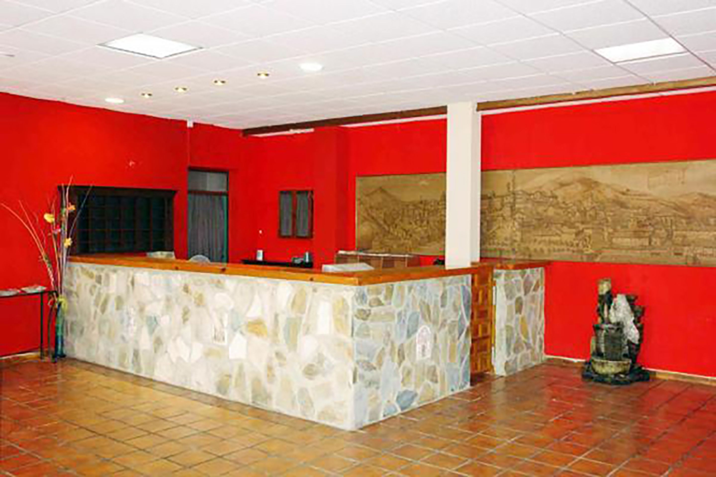 Un área de recepción con mostrador de piedra, paredes rojas y suelo de baldosas.