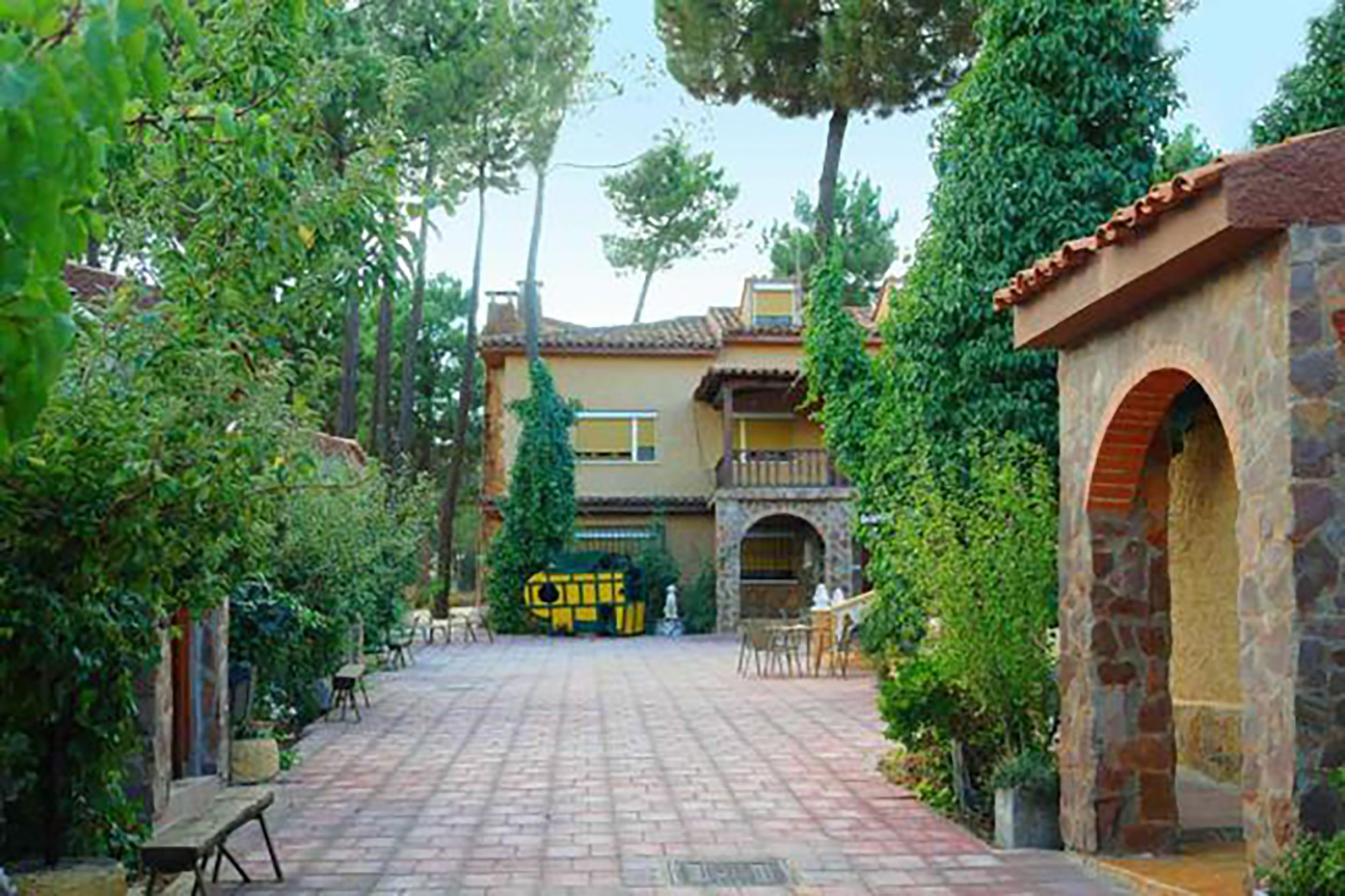 Un patio con un camino empedrado, un arco de piedra y un edificio con un letrero amarillo.