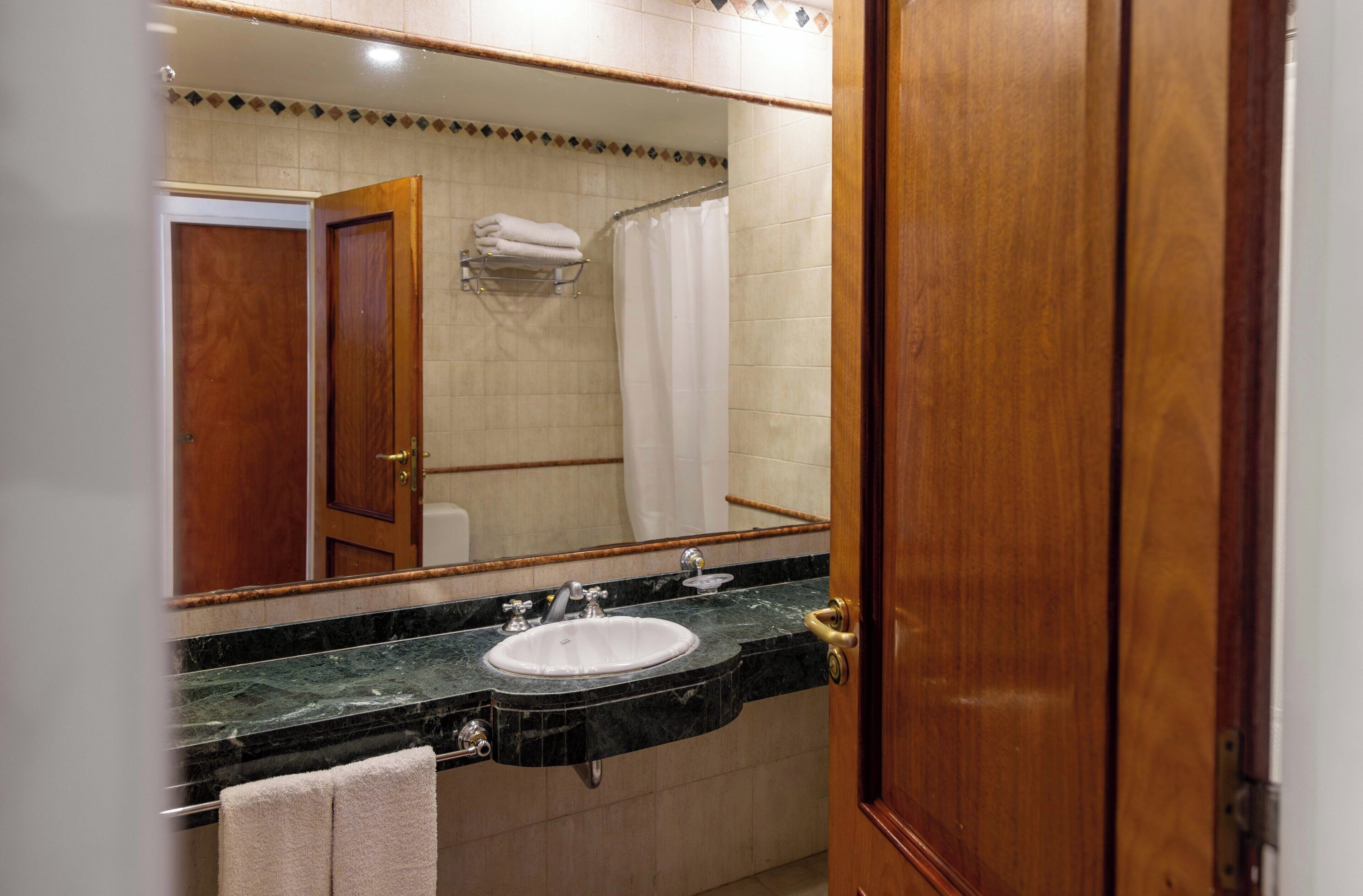 A bathroom with a sink, mirror, and shower curtain.