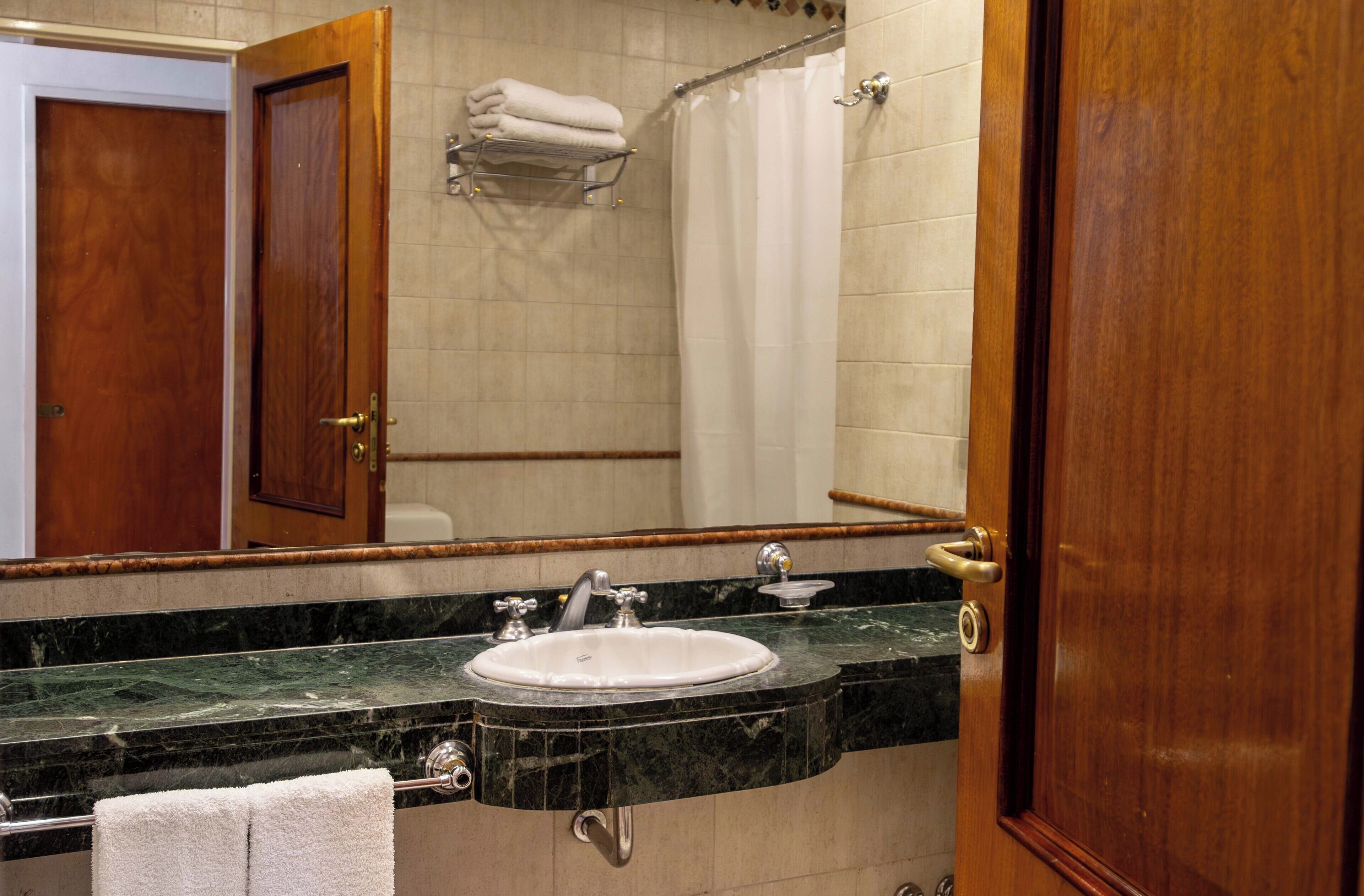 A bathroom with a marble sink, a mirror, a towel rack, and a shower curtain.