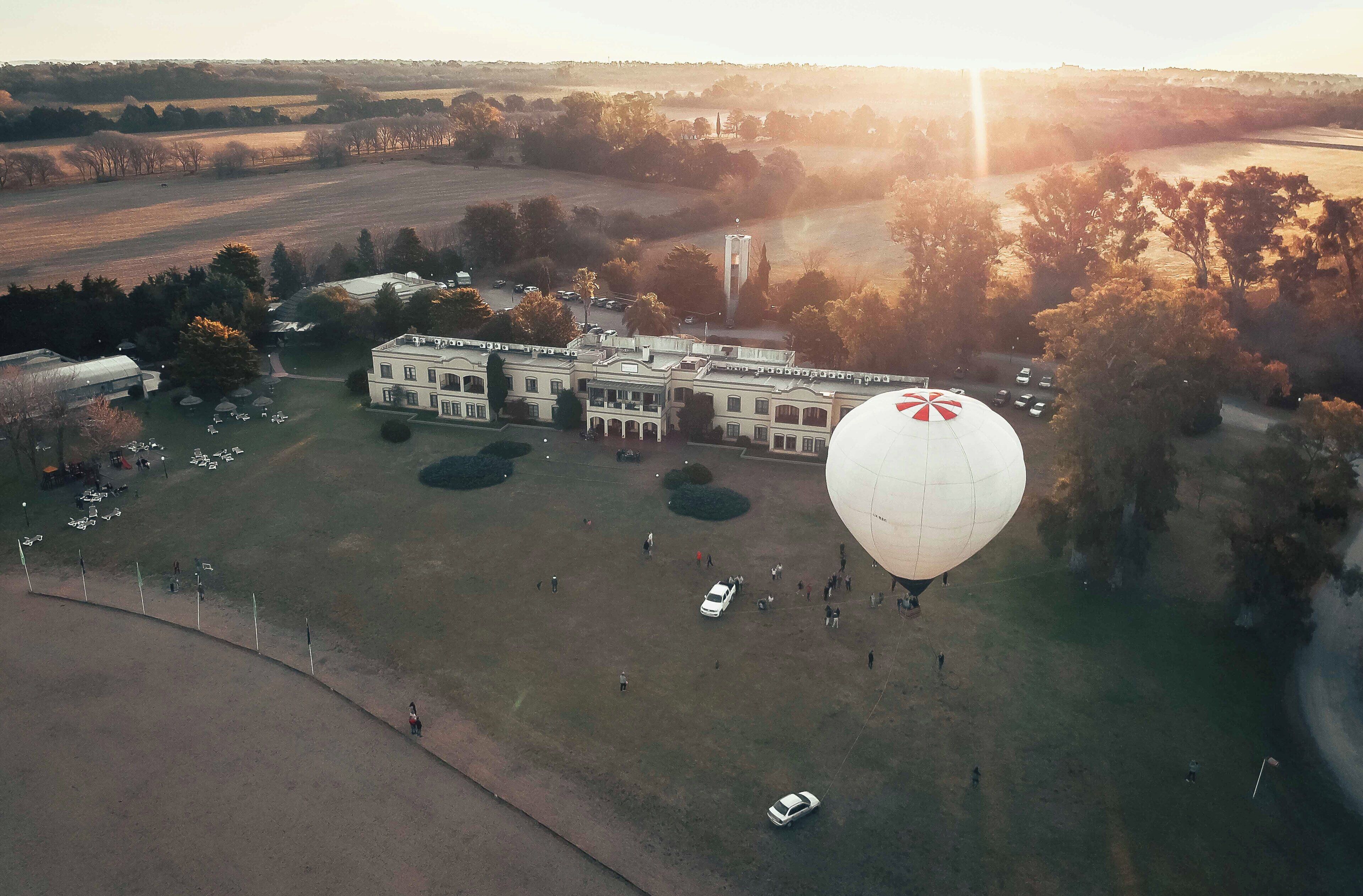 Un edificio grande con un globo blanco llamativo en el techo, rodeado por un área verde con árboles y algunos coches estacionados.