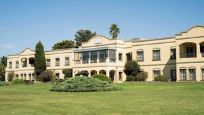 A large, multi-story building with a symmetrical facade, multiple balconies, and a central courtyard with a lawn and trees. - Wyndham Garden Luján (Luján)