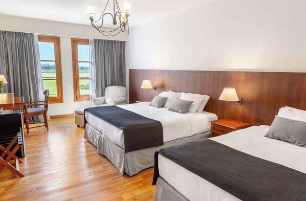 Habitación de hotel con dos camas, un escritorio, una silla y vistas al exterior a través de amplios ventanales.
