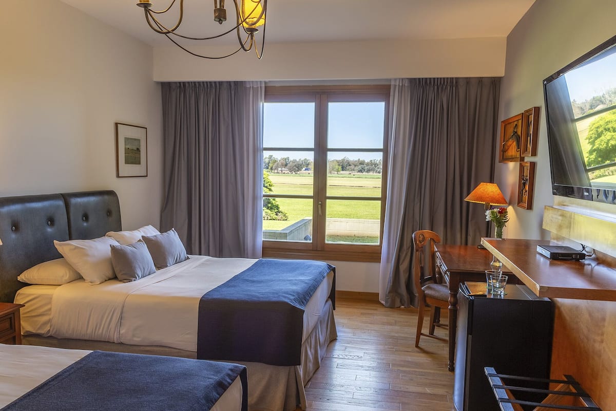 A hotel room with a bed, a desk, a chair, a TV, and a view of the outdoors.