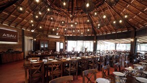 A spacious dining area with wooden tables and chairs, a high ceiling with hanging lights, and a sign reading "ASAU". - Wyndham Garden Luján (Luján)