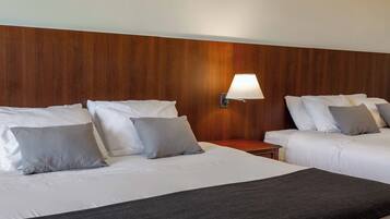 A hotel room with two beds, a wooden headboard, a nightstand, and a wall-mounted lamp.