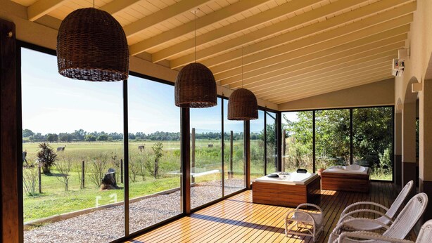 A spacious balcony with wicker chairs, a hot tub, and a wooden deck overlooking a grassy landscape. - Wyndham Garden Luján (Luján)