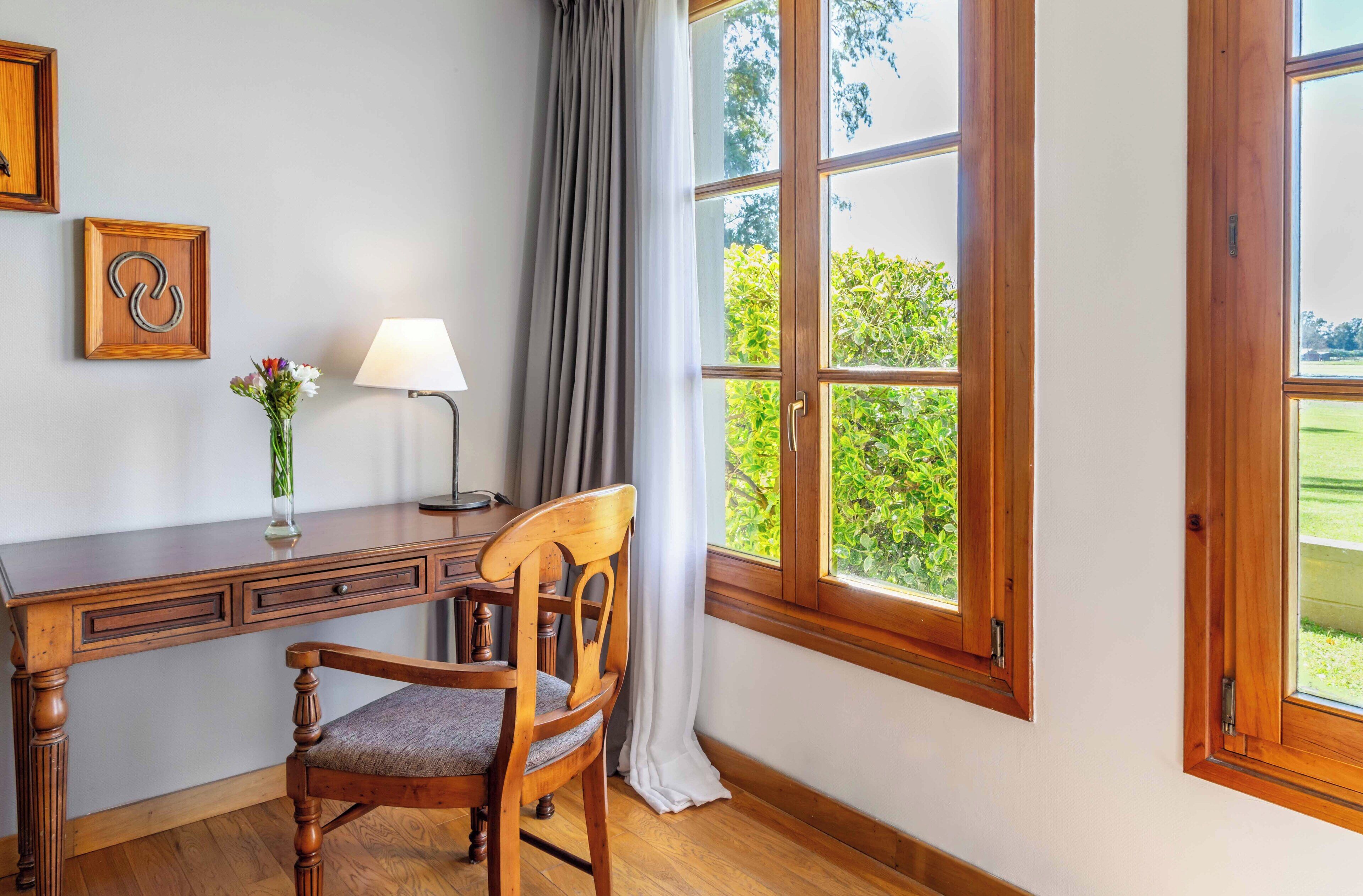 Uma secretária de madeira com uma cadeira, uma lâmpada e um vaso com flores.