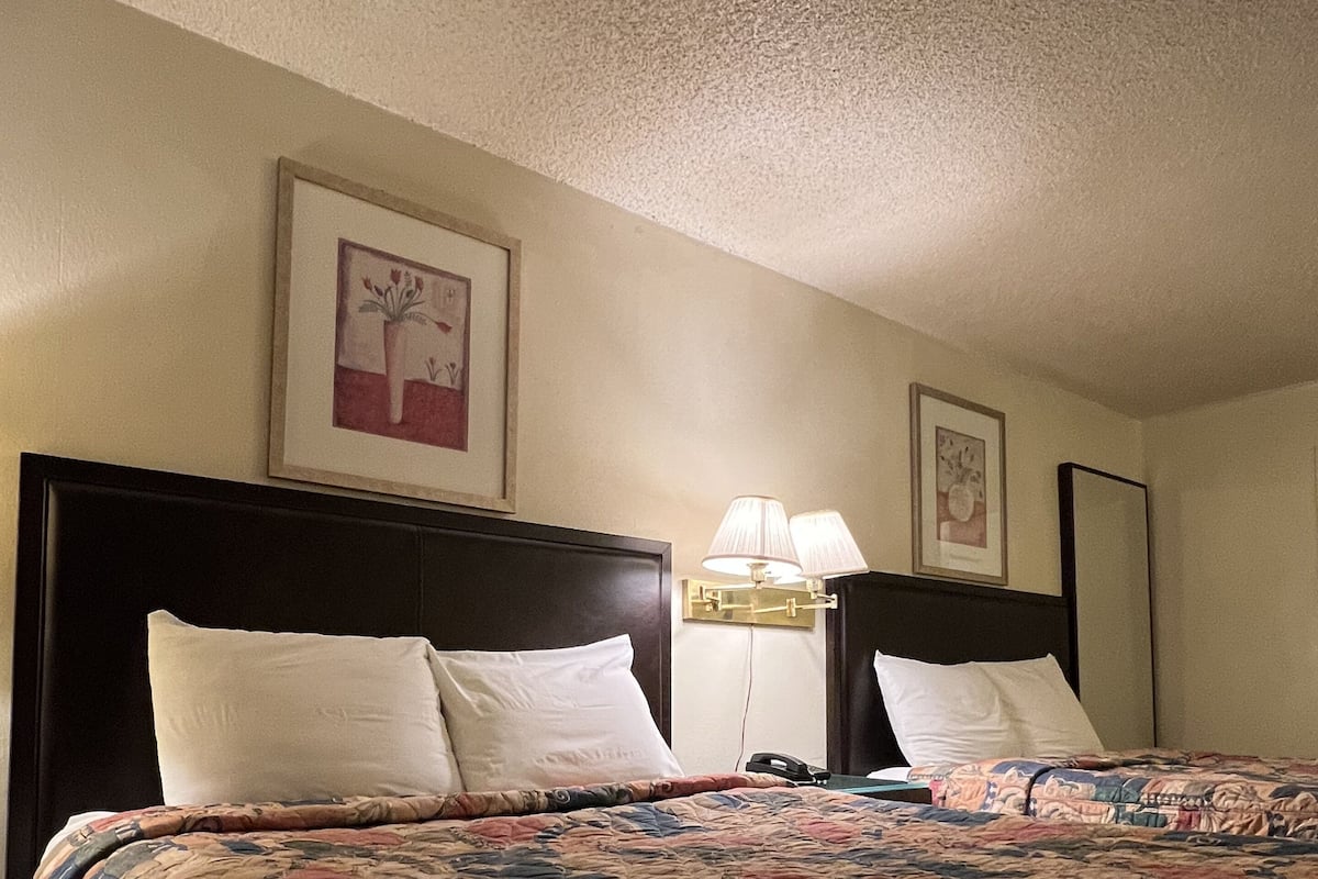 A hotel room with a large bed, two bedside lamps, and two framed pictures on the wall.