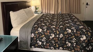 Una camera d'albergo con un letto, un comodino, una lampada, un quadro appeso al muro e una porta.