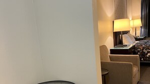 Camera d'albergo con tavolo in vetro, divano, letto con biancheria a fiori e comodino con lampade.