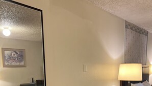 Una camera d'albergo con un grande specchio, un divano, un tavolino, una scrivania con una sedia e un comodino con una lampada.