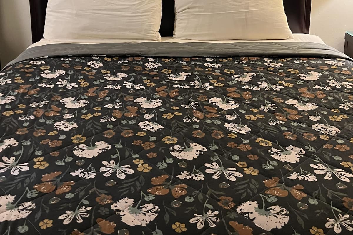 A neatly made bed with a floral-patterned bedspread, a dark headboard, and a framed picture above it.