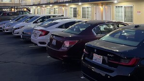 Un motel con diverse camere, un parcheggio e una fila di auto parcheggiate.