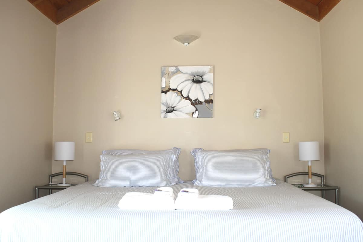 Un dormitorio con una cama grande, dos mesitas de noche con lámparas y una obra de arte en la pared con motivos florales.