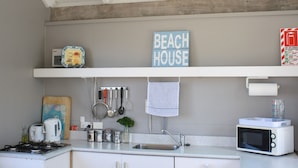 A kitchen with a gas stove, a microwave, a sink, and various utensils. There is a sign that reads "BEACH HOUSE" and a small plant on the counter.