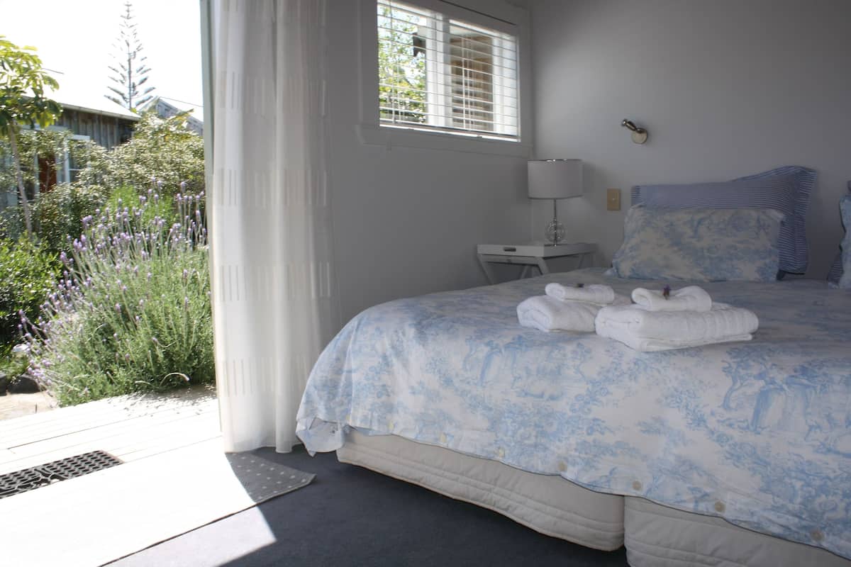 Un dormitorio con una cama grande, una mesita de noche con lámpara y vistas a un jardín.