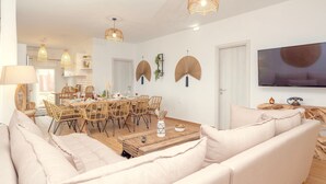 Een moderne woonkamer met een bank, een eettafel en stoelen. Er is een televisie aan de muur bevestigd en een houten salontafel.