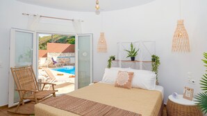 Een slaapkamer met een bed, een stoel, een nachtkastje, een klok en uitzicht op een buitenzwembad.