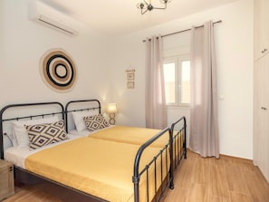 A double bed with a yellow bedspread, a bedside lamp, and a wall clock. - Sky (Rethymno)