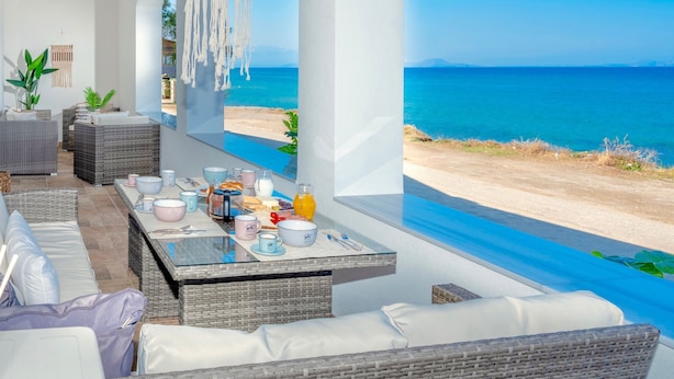 Een eetgedeelte aan zee met rieten meubels, een glazen tafel en uitzicht op de oceaan.