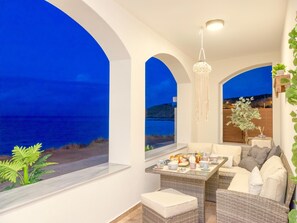 Un coin salon confortable avec vue sur la mer, une table à manger dressée et un luminaire suspendu.