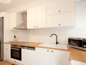 A modern kitchen with white cabinets, a stainless steel range hood, a dishwasher, an oven, a sink with a black faucet, and a microwave. - Sky (Rethymno)