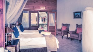 Een kamer met een bed, twee fauteuils, een tafeltje en een schilderij aan de muur.