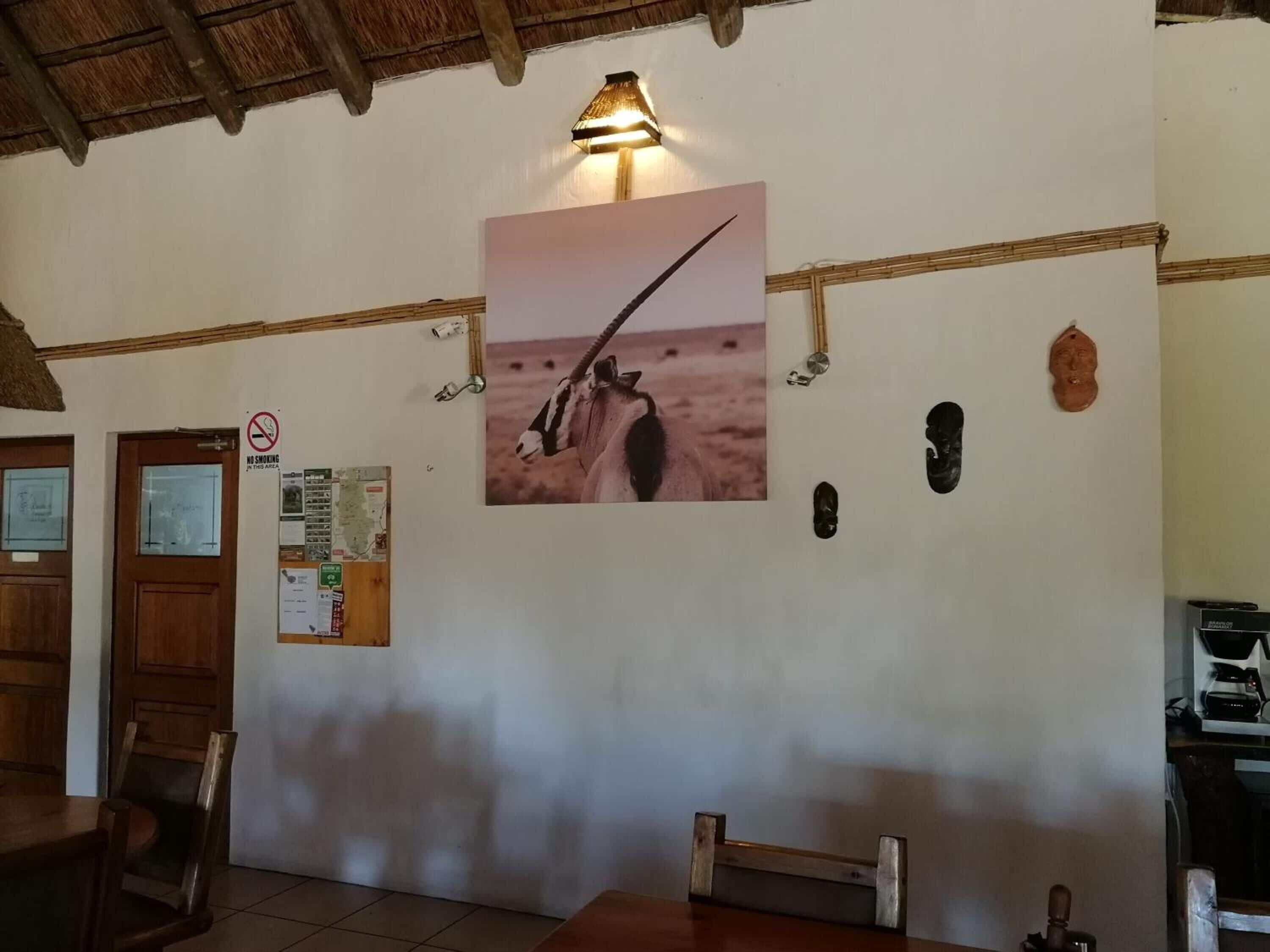 Una habitación con techo de madera, una lámpara de pared, un cuadro enmarcado de un animal, un cartel de prohibido fumar y un tablón de anuncios con varios avisos.