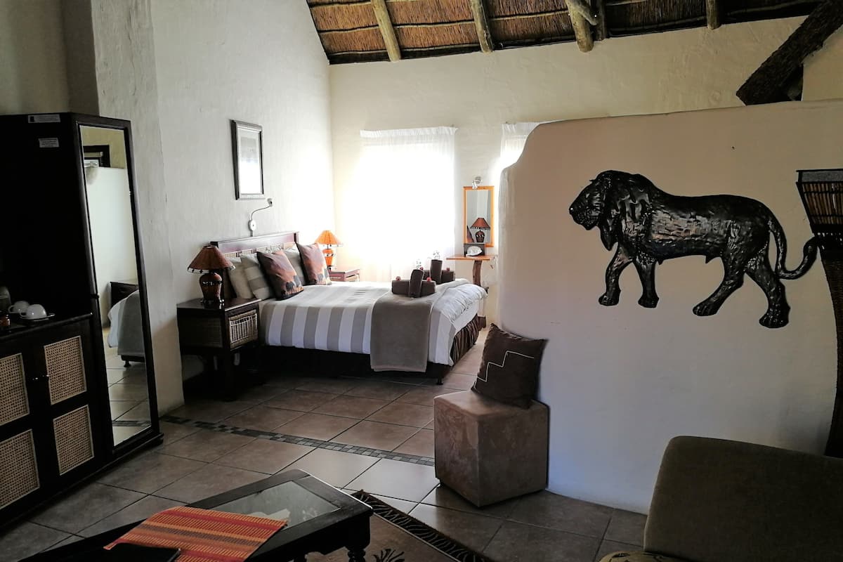 A room with a bed, a sofa, a small table, and a wall-mounted artwork of a lion.