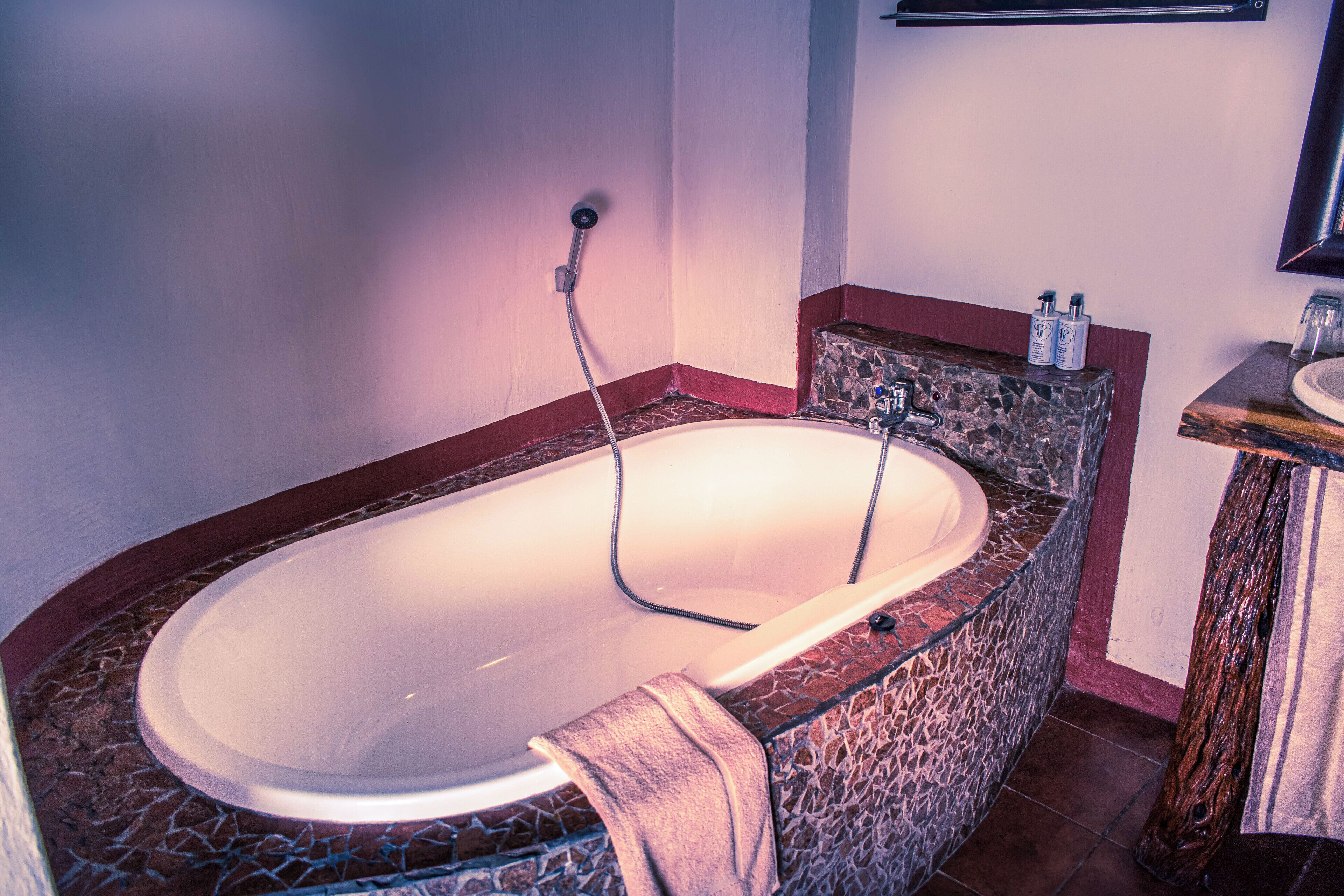 Ein Badezimmer mit einer freistehenden Badewanne, einem marmorverkleideten Duschbereich und einem Holzwaschtisch mit Spüle und Handtuchhalter.