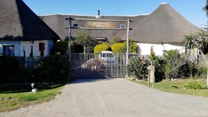 Een lodge-ingang met rieten dak, een bord met de tekst 'Elephants Foot Lodge', en een omheind gebied met een olifantbeeld.