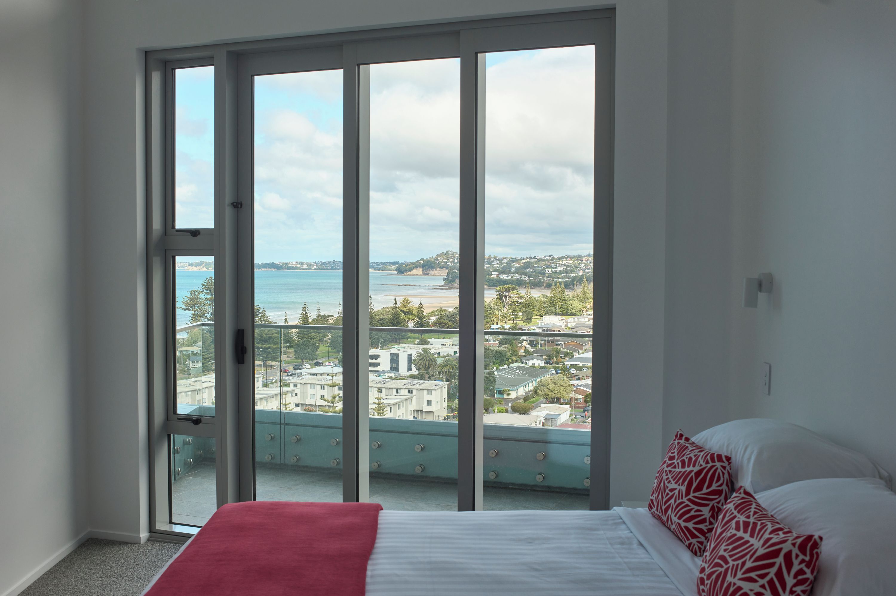 Un dormitorio con un amplio ventanal corredera que da a un balcón con vistas a la ciudad.
