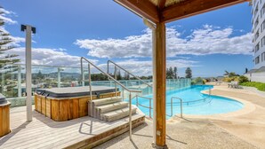 A wooden deck with a hot tub, stairs leading to a pool, and a glass railing. - Marsden Suites Nautilus Orewa (Orewa)