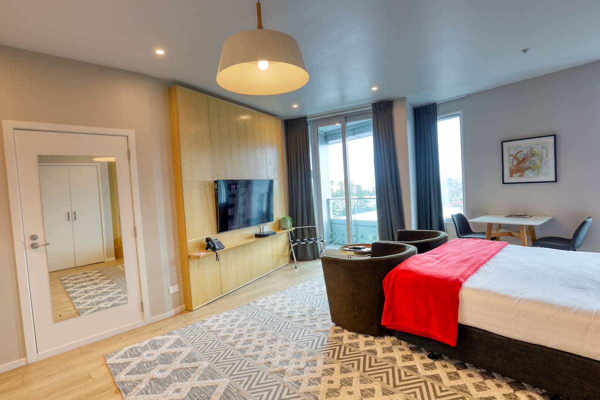 A modern hotel room with a large bed, a television, a desk, and a view of the city.