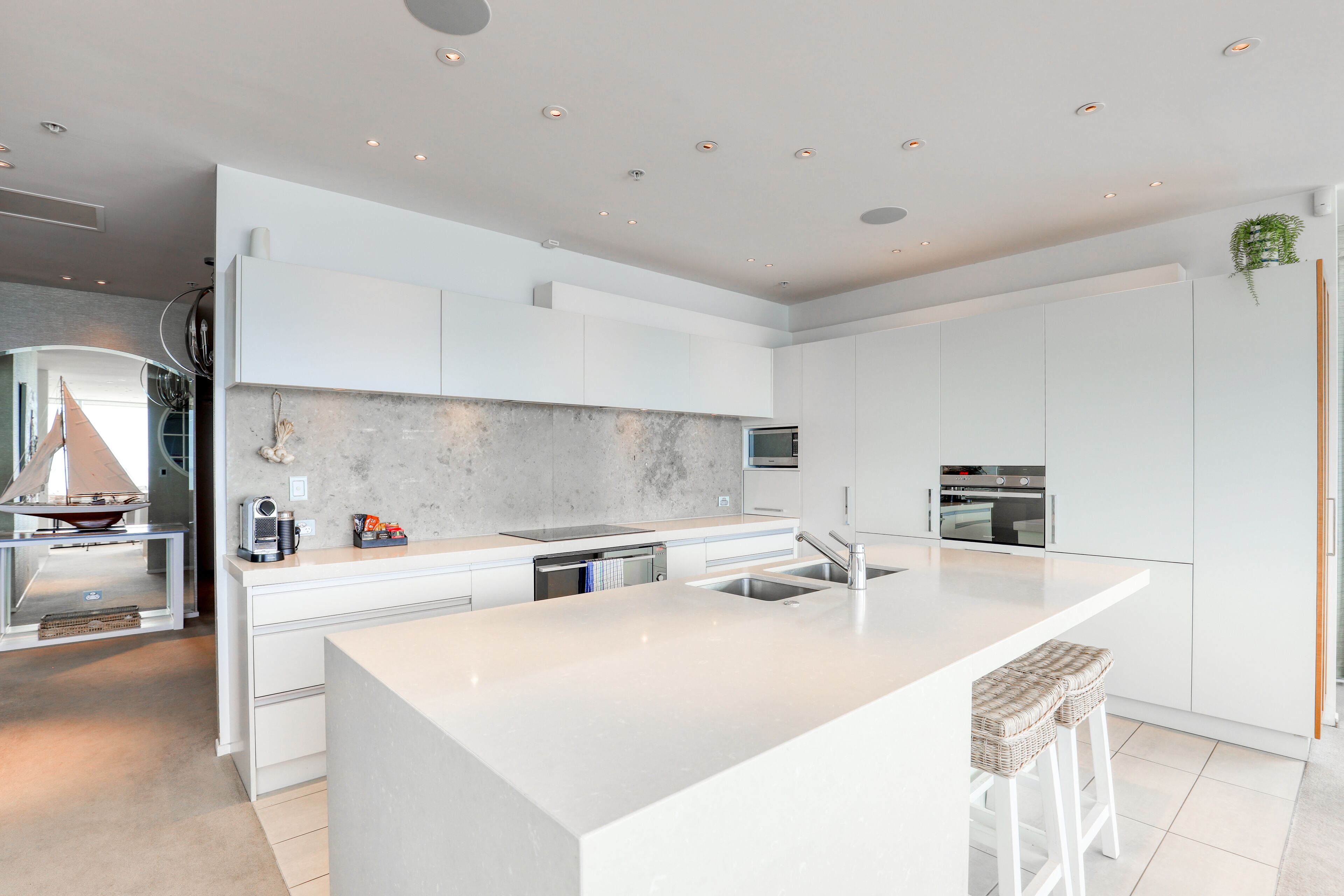 Une cuisine moderne avec des meubles blancs, un grand îlot central, des appareils en acier inoxydable et un four encastré.