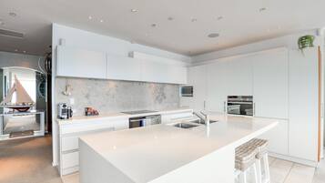 Une cuisine moderne avec des meubles blancs, un grand îlot central, des appareils en acier inoxydable et un four encastré.