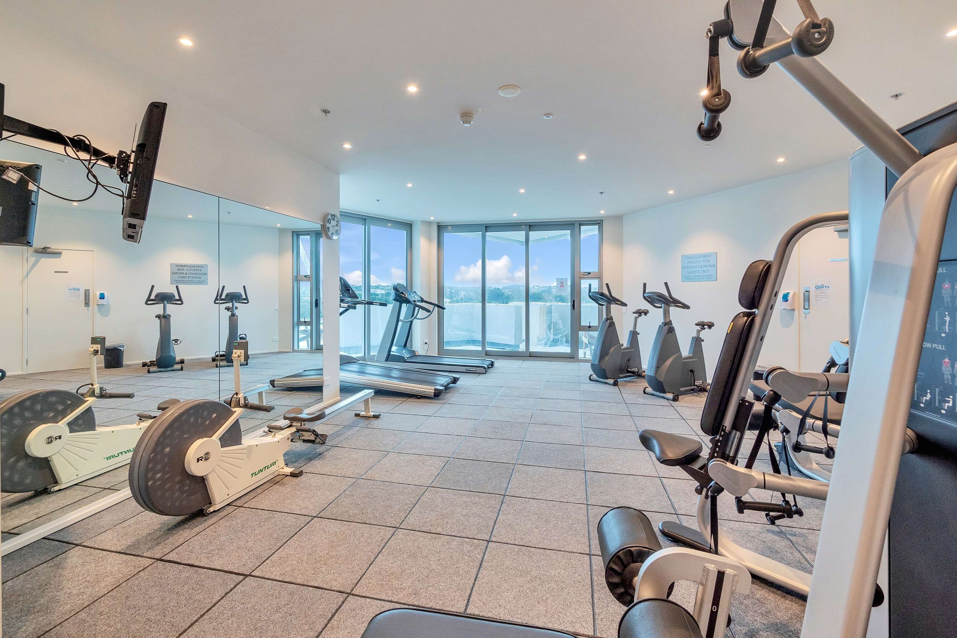 Ett modernt gym med olika typer av träningsutrustning, stora fönster och utsikt över staden.