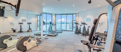 Ett modernt gym med olika typer av träningsutrustning, stora fönster och utsikt över staden.