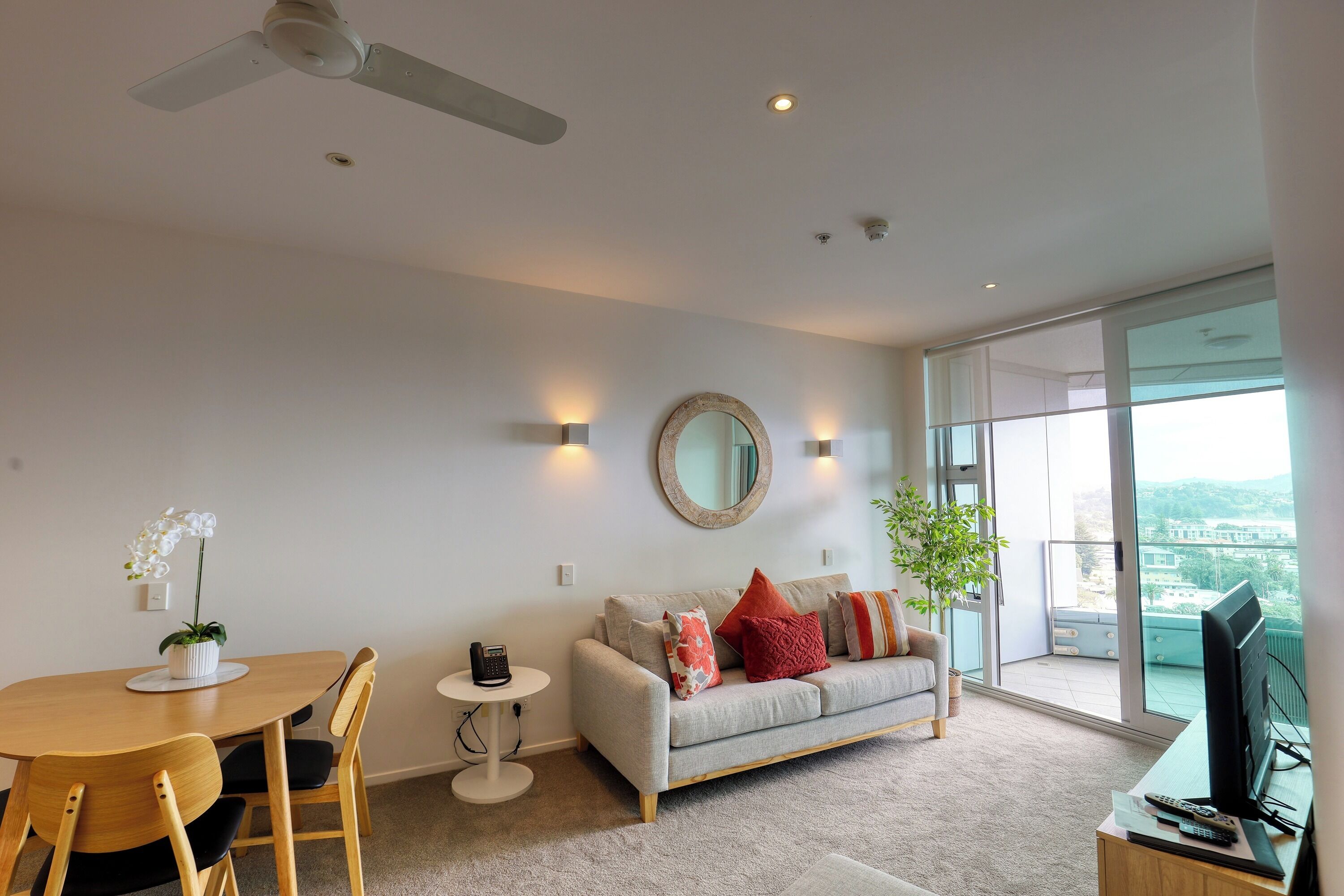 A modern living room with a dining table, sofa, and a large window offering a city view.