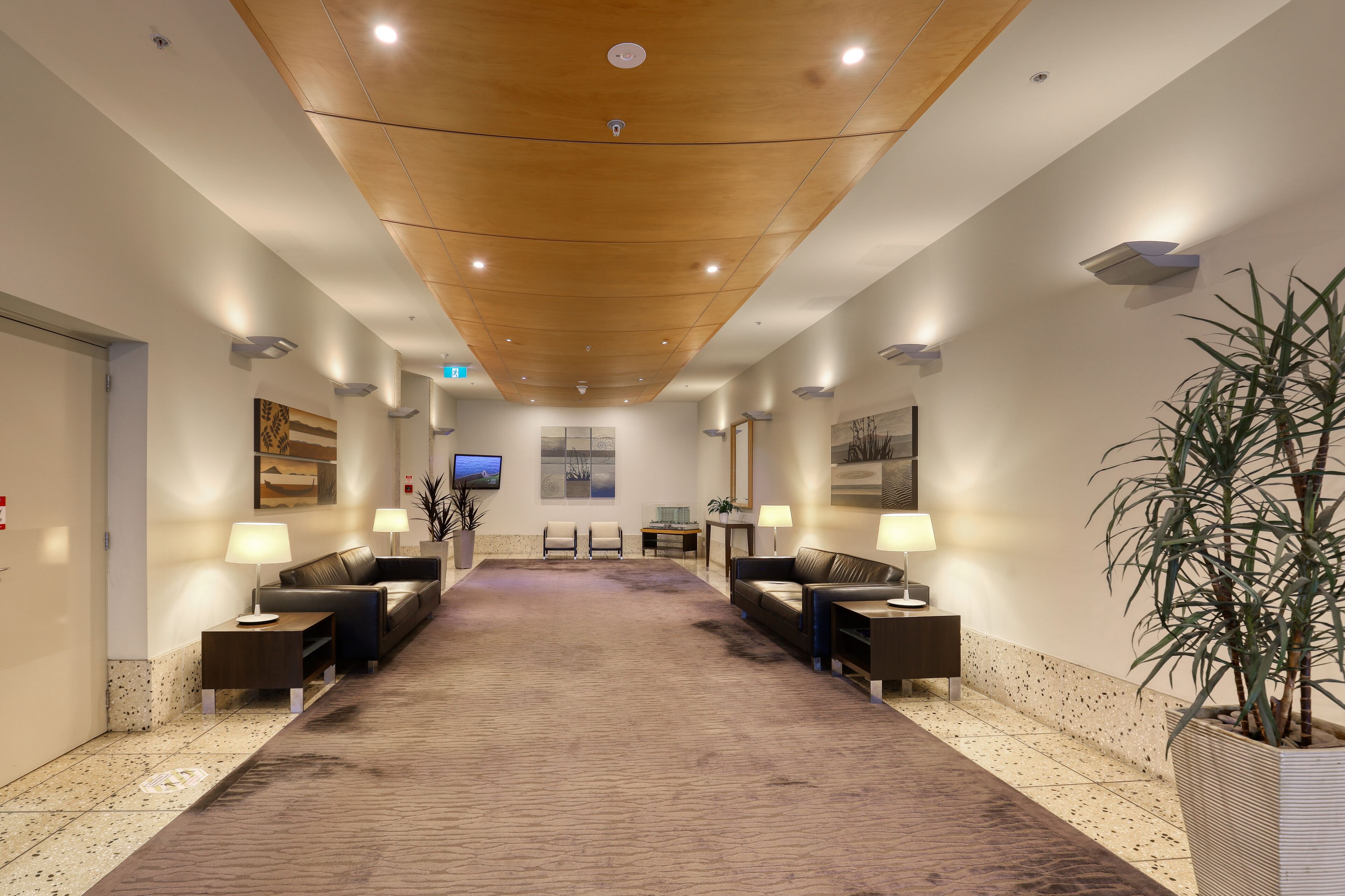 A hotel lobby with a long carpeted area, two sofas, a reception desk, and a television on the wall.