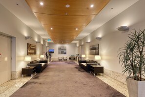 A hotel lobby with a long carpeted area, two sofas, a reception desk, and a television on the wall. - Marsden Suites Nautilus Orewa (Orewa)