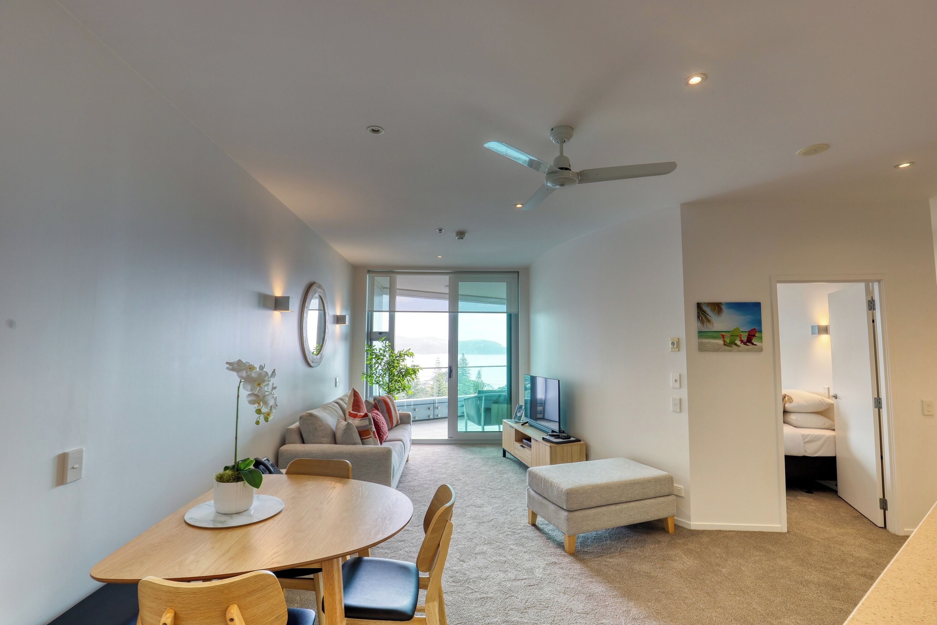 A modern living room with a dining area, a sofa, a TV, and a balcony with a view.