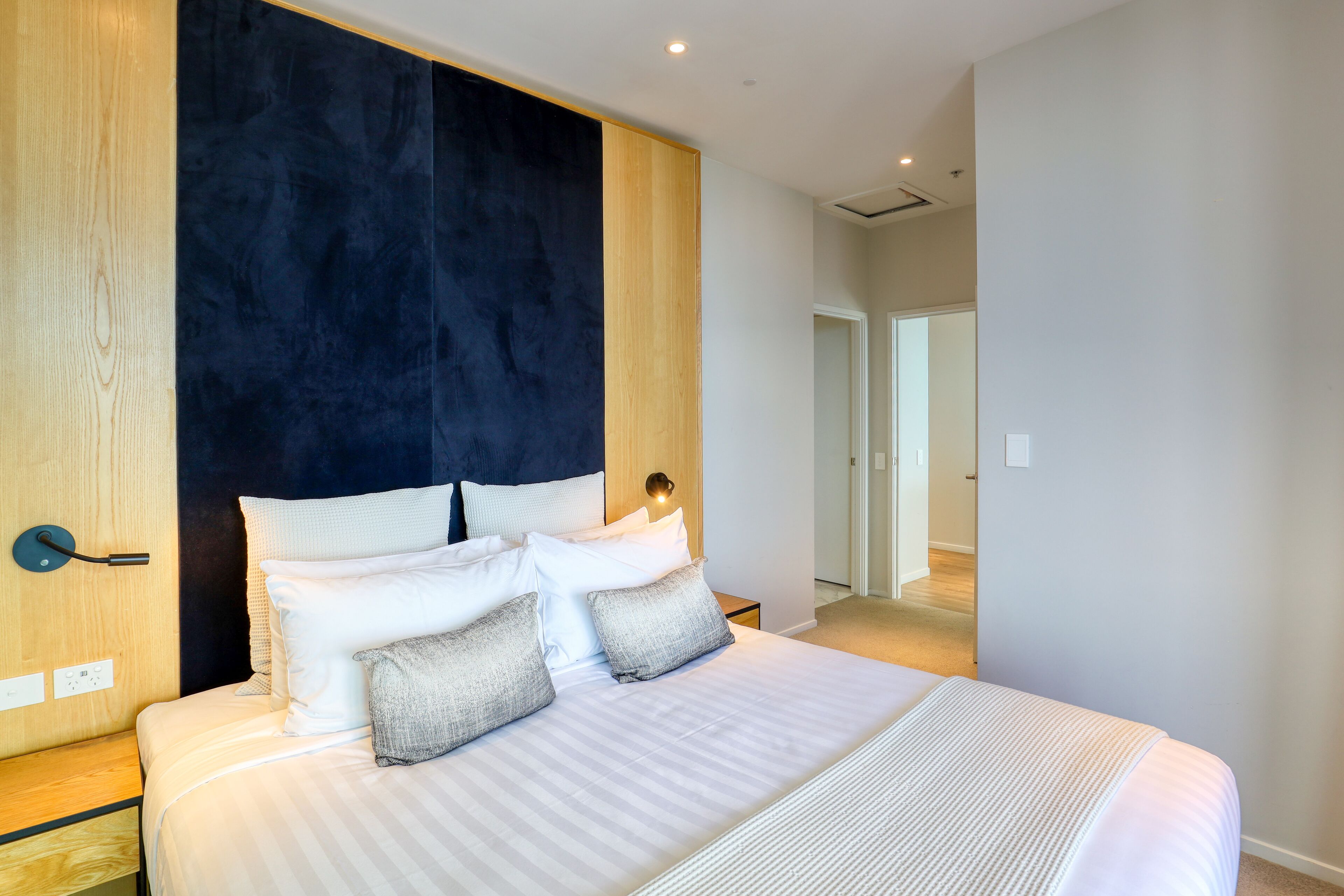 Un dormitorio moderno con una cama grande, una pared de acento oscura y un panel de madera a la izquierda.