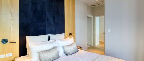 Un dormitorio moderno con una cama grande, una pared de acento oscura y un panel de madera a la izquierda.