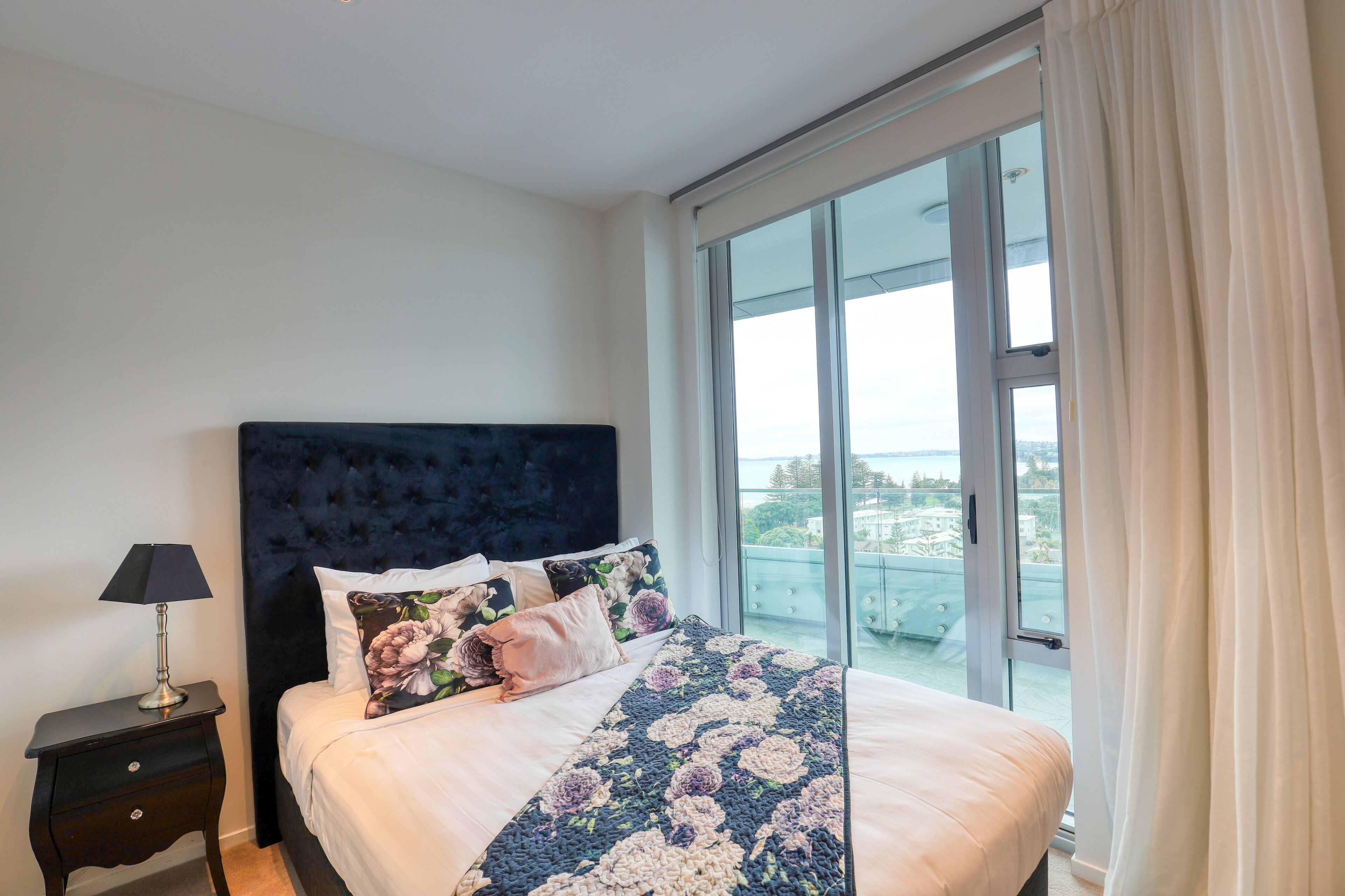A bedroom with a large bed, a nightstand, and a window with curtains.