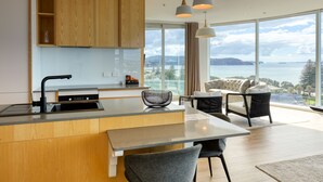 A modern kitchen with wooden cabinets, a built-in island, and a dining area with a view of the sea. - Marsden Suites Nautilus Orewa (Orewa)