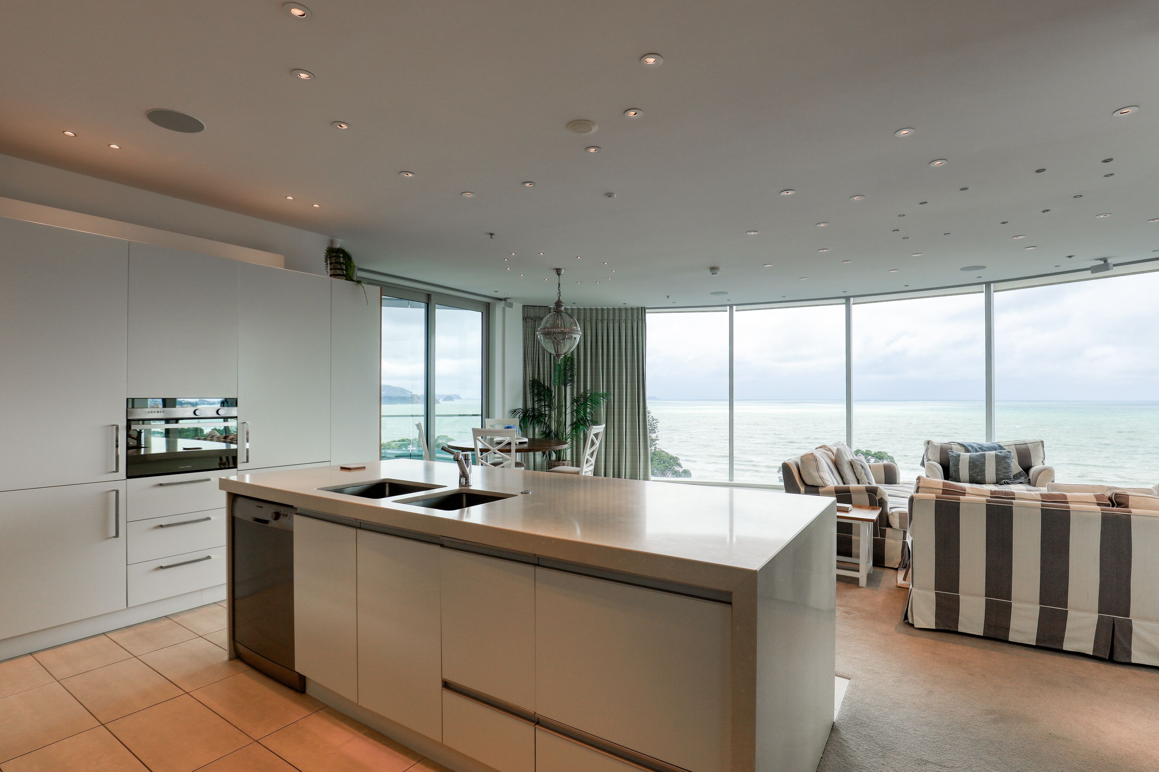 A modern kitchen with a large island, a dining area with a view of the sea, and a cozy seating area with a striped sofa.