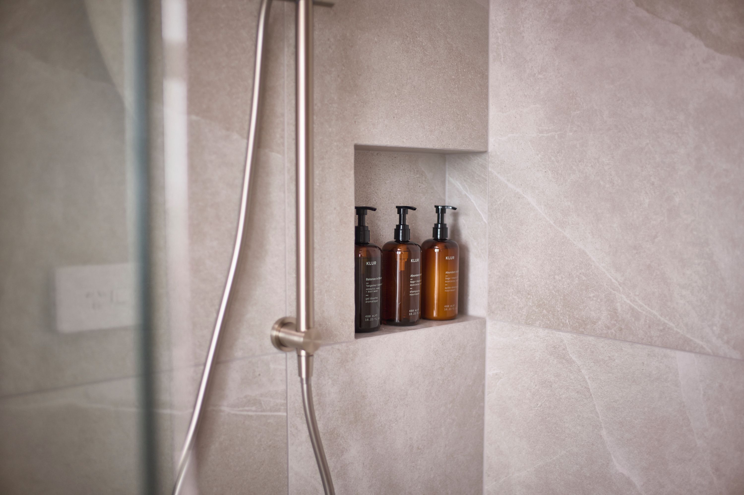 A shower enclosure with a built-in shelf holding three bottles of shampoo.